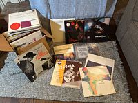 Wide view showing the box filled with multiple vinyl record albums with some albums laid out in front including jazz, classical, and flamenco music records.