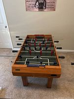 Overview of wooden foosball table with visible red and blue player figures on rods.