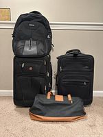 LIWAG backpack stacked on two black expandable suitcases, with Elizabeth Arden bag in front