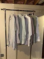 Photo of eight men's dress shirts hung on a metal rack in a basement or storage area, various striped patterns.