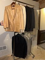 Eight men's jackets and coats including leather, fabric sport coats and suits hung on racks, some in protective covers