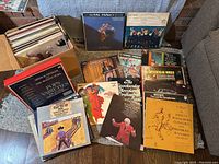 Box of approximately 60 records with many boxed sets and loose albums arranged on a couch and floor.