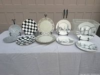 Photo of 10 decorative plates showing various designs including checkerboard, floral, and vintage ship prints with plastic storage bin behind