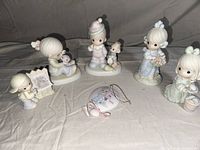 Seven Precious Moments figures arranged on beige fabric background, showing all figurines clearly.