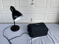 Black table lamp and InFocus projector in carrying case on table, with power cord attached.