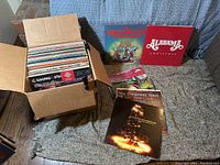 Box of approximately 60 vinyl Christmas records by various artists from different eras, displayed with some album covers outside the box for clear identification.
