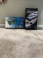 Photo of boxed tabletop billiard and air hockey games side by side on carpet
