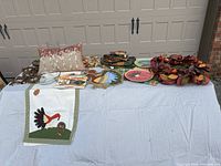 Full view of the lot on a white tablecloth showing textiles, plates, wreath, pillow, and books
