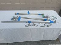 Photo of various metal curtain rods, tie backs, mounting brackets, and hardware laid out on a white table indoors.