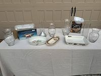 Full lot view showing silver-plated pieces, glass vases, and ceramic casserole dishes on white cloth-covered table in front of garage door.