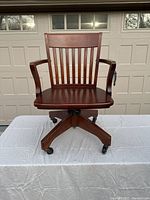Front view of the wooden rolling office chair showing the seat, backrest, armrests, and caster wheels.