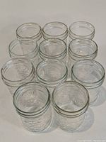 Eleven clear glass mason jars arranged in rows, showing embossed texture on glass surface.