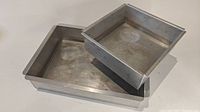 Two aluminum cake pans stacked, larger rectangular under smaller square pan.