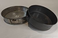 Two springform baking pans shown side by side on a white background; one metal with textured base, one dark-coated, both showing springform latch.