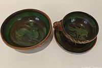 Single view of bowl and cup with saucer showing green animal designs on dark green glaze interior with reddish brown exterior.