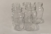 5 clear glass mason jars viewed from front and side, showing embossed brand text and wide openings
