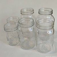 Photo showing six clear glass wide-mouth mason jars with embossed designs, displayed in two rows.