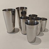 Seven stainless steel cups arranged together on a light surface, two noticeably larger than the rest.