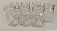Front view of seven clear glass mason jars with embossed writing, arranged on a white background.