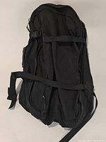 Black bag laid flat showing back side with padded area and adjustable straps for backpack use.