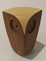 Front angled close-up of wooden owl, showing carved circular eyes and smooth wood grain with light colored flat top.