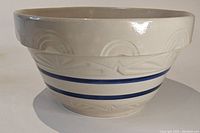 Side view of the beige/cream ceramic bowl showing embossed patterns and two blue stripes.