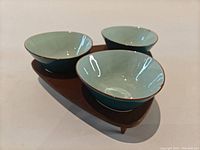 Photo showing the three ceramic bowls inset into the wooden stand, highlighting the pale interior glaze and overall shape.