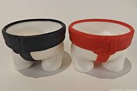 Front angle of two sumo-wrestler egg cups showing black and red mawashi detail.