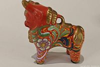 Side view of red ceramic bull figurine with painted floral patterns and gold highlights