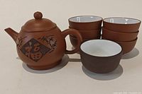 Photo showing the tiny Chinese red clay teapot with six stacked cups and one cup placed separately in front.