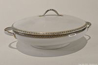 Side angle image of the ceramic serving dish showing decorative border and lid with handle.
