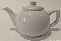 Front view of white ceramic teapot showing short spout, round body, and handle.