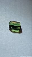 Close-up image of a bright green octagon cut natural tourmaline gemstone placed on a light fabric background.