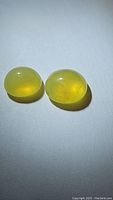 Two oval cabochon cut natural African yellow fire opals placed side by side, showing smooth polished surfaces with yellow translucent color and some internal inclusions.