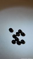 Photo showing cluster of small polished black onyx cabochon beads on white background.