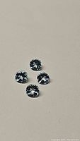 Four round, light blue gemstones arranged on a plain gray surface, showing facets and brilliance, size calibrated to 4mm.