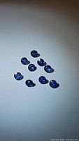 Top view showing ten natural round cut blue sapphires arranged on a white background under lighting that highlights their color and cut.