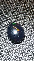 Close-up photo of the oval Ethiopian black opal cabochon showing rainbow flashes on black base material.
