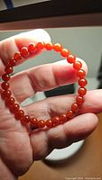 Front view of the fire red Carnelian bracelet, showing the round, polished beads held in the hand.