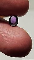 Close-up image of the 1.06 carat oval cabochon purple amethyst held between fingers, highlighting color and inclusions.