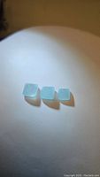 Three cushion cut untreated blue aquamarine gemstones arranged in a row on a plain surface under direct light showing color and transparency.