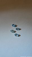 Four small oval cut blue zircon gemstones laid on flat surface showing light sky blue color and good clarity.