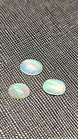 Three oval translucent to semi-translucent natural Ethiopian opals with bright rainbow flashes lying on a dark textured fabric background.
