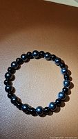Photo of natural gemstone stretchy bracelet composed of polished 6mm jet black onyx beads and shiny 8mm hematite beads arranged in a circle on a brown surface.