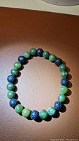 Front view of stretch bracelet with alternating green jade and black lava stone beads on a brown surface