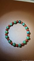 Natural gemstone bracelet photographed on a brown surface, showing alternating green jade and fire red carnelian beads.
