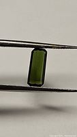 Close-up photo of natural green octagon-cut tourmaline gemstone held by tweezers showing clarity and color.
