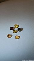 Seven round cut multicolored sapphires in yellow, purple, and dark greenish tones arranged on a white surface with light shadowing.