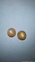 Pair of natural round peach moonstone cabochon gemstones on light fabric background showing color and chatoyancy.
