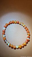 Top-down photo showing the full circular stretchy bracelet of red agate beads on a light brown background with visible bead pattern and color.